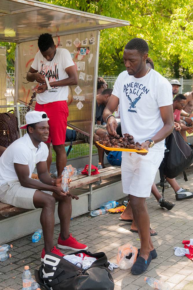 Olabode, who recently got married, hands out barbecued chicken to his friends in the park. West African football migrants often hold informal parties in the park. Weddings, the birth of children, and other important occasions are celebrated with food, drinks, music and dances. Warsaw, Summer 2016. (Photo Paweł Banaś)