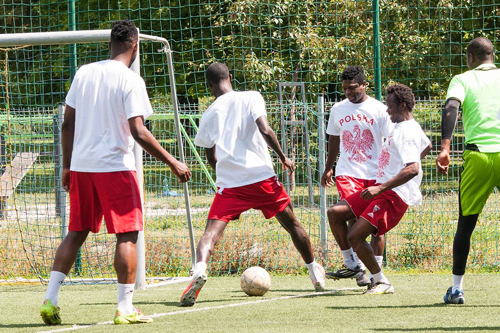 West African football players who currently play in Poland warm up before a friendly game with former players doing rondo, a popular practice in which a group of players standing in a circle pass the ball to one another while two footballers in the middle of the circle try to intercept the ball. Warsaw, Summer 2016. (Photo Paweł Banaś)